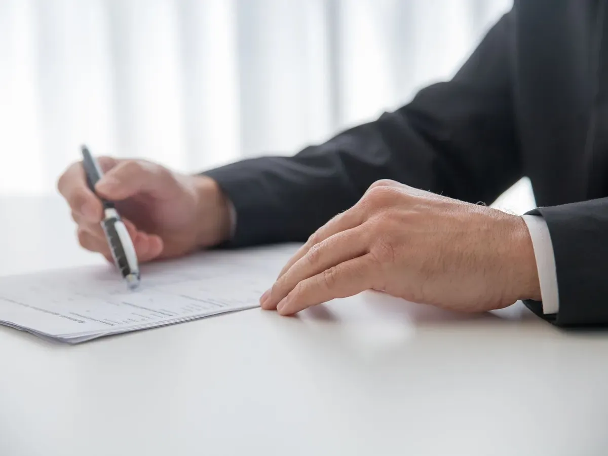 Manos firmando un documento sobre una mesa blanca de oficina